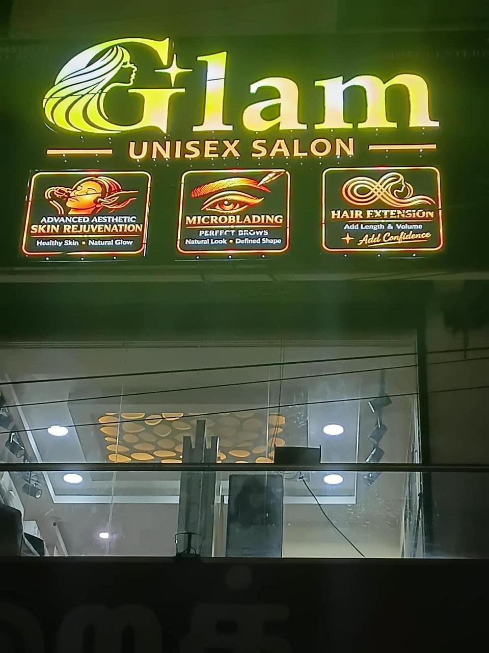 The illuminated GLAM Unisex Salon signboard at night